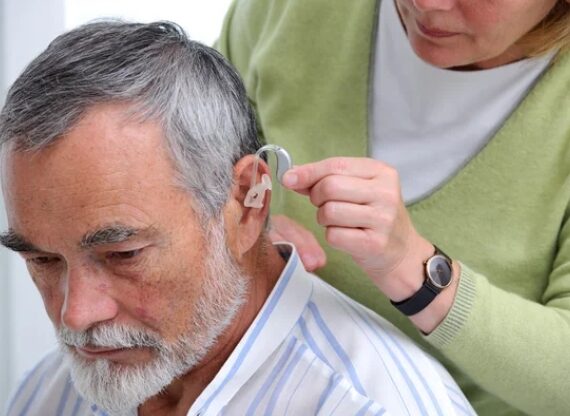 A doctor fitting a hearing aid into a man’s ear